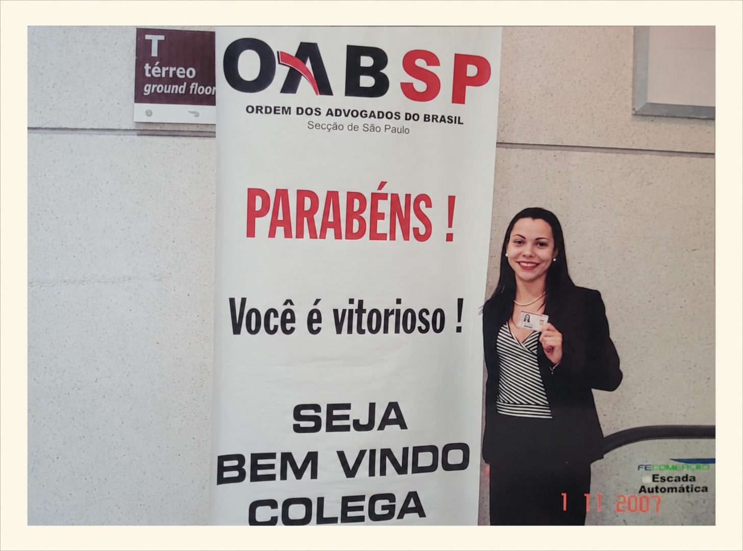 Paloma Correia em frente ao banner de boas-vindas da OAB/SP, segurando sua carteira da Ordem, em 2007.